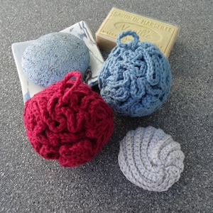 Può includere: Quattro pouf da bagno all'uncinetto in diversi colori: rosso, blu, grigio e blu chiaro. I pouf sono su una superficie grigia.