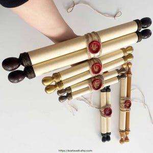Op de afbeelding: Verschillende opgerolde perkamentrollen met houten handvatten en rode zegels worden getoond. De rollen zijn vastgebonden met touw. De handvatten zijn donkerbruin, goud en zwart. Het perkament is lichtbruin van kleur.