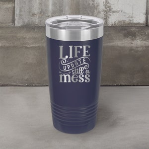 May include: A navy blue stainless steel tumbler with a silver lid. The tumbler has the text "LIFE UPDATE still a mess" engraved on the side.