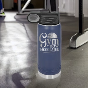May include: A blue stainless steel water bottle with a black lid and a silver inscription that reads "Gym now Tacos later".