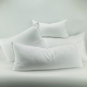 May include: Four white pillows stacked on top of each other. The pillows are all rectangular and have a smooth, white fabric cover.