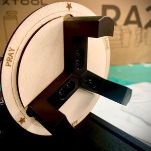 Puede incluir: Primer plano de un plato giratorio de madera con un accesorio de metal de tres puntas. El plato giratorio est&aacute; etiquetado con las palabras "Rezar", "Amar" y "Levantar".