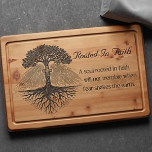 May include: Wooden cutting board with a carved tree design and the words "Rooted In Faith." The tree has a cross incorporated into the trunk. The board also has an inscription about faith.