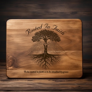 May include: A rectangular wooden cutting board with rounded corners. The board features an engraved tree design with a cross, the words "Rooted In Faith", and the phrase "To be rooted in faith is to be steadied by grace".