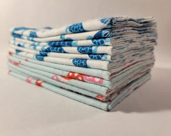May include: A stack of folded fabric cloths with a blue and white pattern on one side and a pink and red pattern on the other side.
