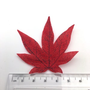 May include: A single red fabric maple leaf with a black vein pattern. The leaf is approximately 4 cm wide.