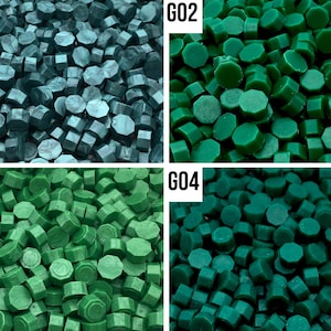 May include: Four different shades of green sealing wax. The wax is in the shape of small, round pellets. The colors are teal, forest green, dark green, and a lighter shade of green.