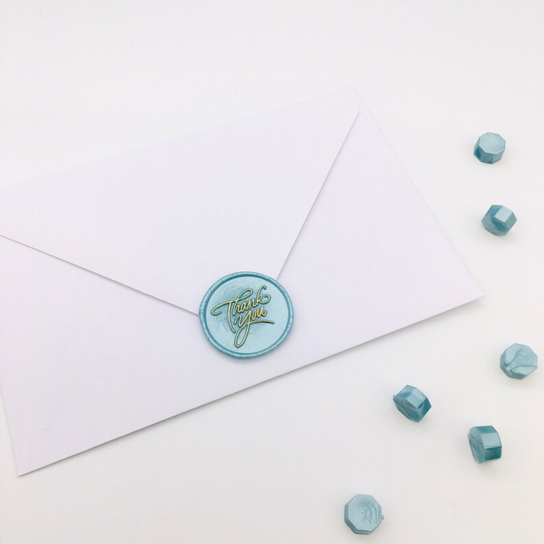 May include: A white envelope with a blue wax seal that says "Thank You" in gold lettering. There are several blue wax seals scattered around the envelope.