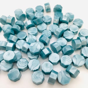 May include: A collection of light blue hexagonal wax seals. The seals have a marbled effect and are scattered on a white surface.