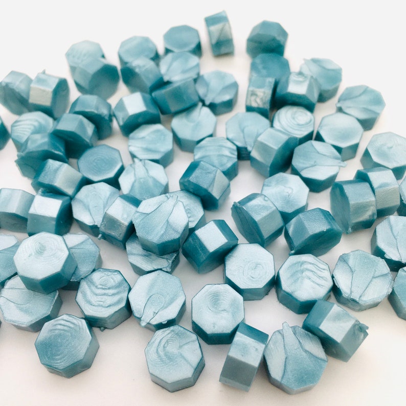 May include: A collection of light blue hexagonal wax seals. The seals have a marbled effect and are scattered on a white surface.