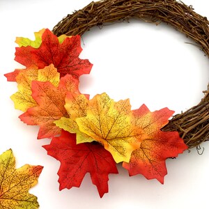 May include: A fall-themed wreath with a brown vine base and orange, yellow, and red maple leaves.