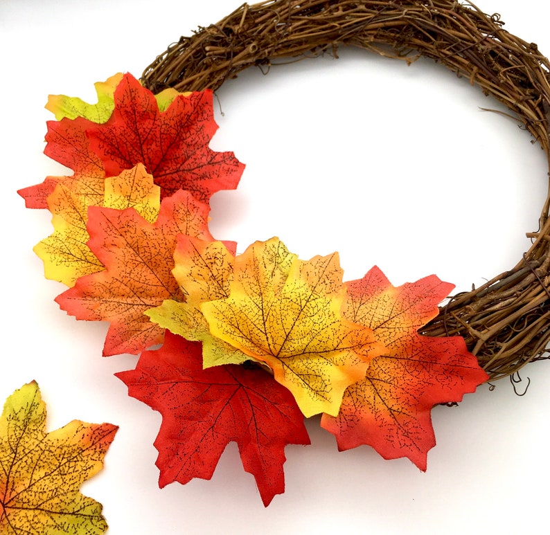 May include: A fall-themed wreath with a brown vine base and orange, yellow, and red maple leaves.