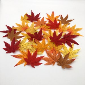 May include: A collection of artificial maple leaves in various shades of red, orange, and yellow. The leaves are scattered on a white background.