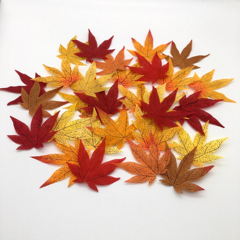 May include: A collection of artificial maple leaves in various shades of red, orange, and yellow. The leaves are scattered on a white background.
