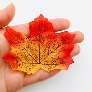 May include: A single, artificial maple leaf with a detailed vein pattern. The leaf is orange, yellow, and red.