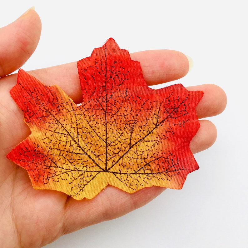 May include: A single, artificial maple leaf with a detailed vein pattern. The leaf is orange, yellow, and red.