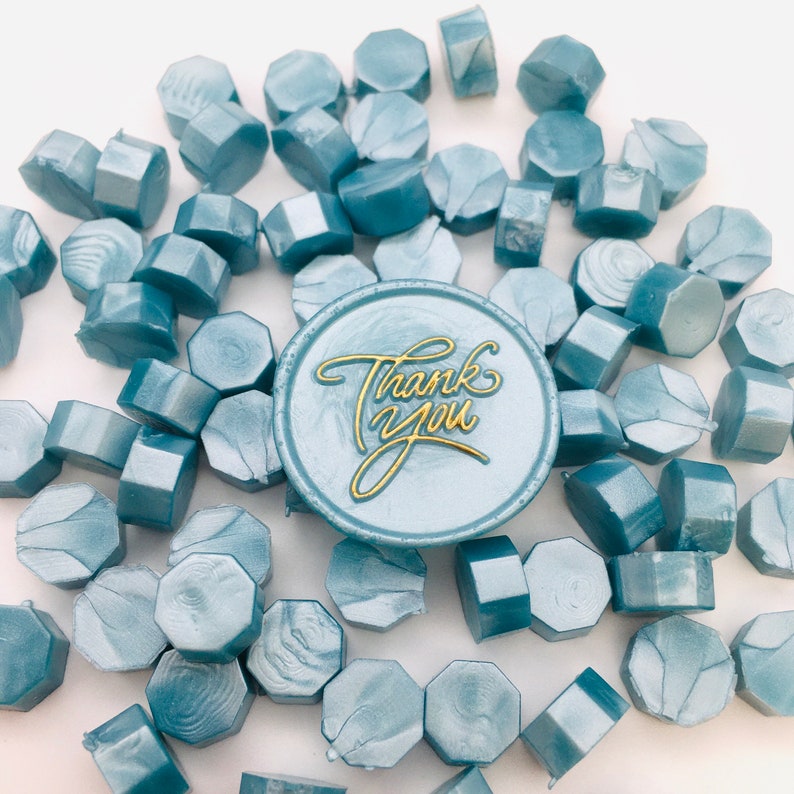 May include: A close-up of a blue wax seal with the words "Thank You" written in gold lettering. The wax seal is surrounded by many other blue wax seals.