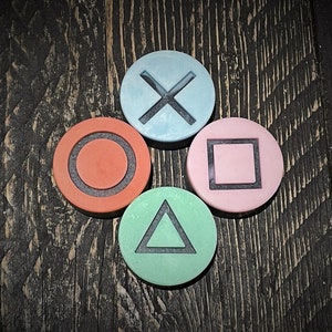 May include: Four colourful round coasters with different symbols: a circle, a triangle, a square, and an X. The coasters are on a dark wood surface.