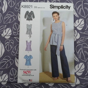 May include: Simplicity sewing pattern K8921, size D5 UK 8-16, featuring four different styles of tops. The pattern includes a sleeveless top with a tie waist, a top with a gathered neckline and short sleeves, a top with a V-neck and short sleeves, and a top with a wrap neckline and short sleeves. The pattern is produced in association with Sew magazine.