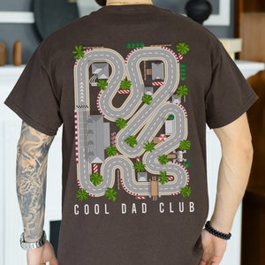 May include: A brown t-shirt with a graphic of a race track with palm trees and the text "COOL DAD CLUB".