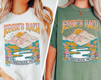 May include: Two t-shirts featuring a mountain scene and the text "Jessie's Bach 20 Innscruck, MO 24" printed on the front. The t-shirts are white and moss green.