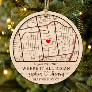 May include: A round wooden ornament with a map design, a red heart, and the text "August 28th 2025 WHERE IT ALL BEGAN Sophia Henry Glastonbury, CT." The ornament hangs from a natural twine string, perfect for a Christmas tree.