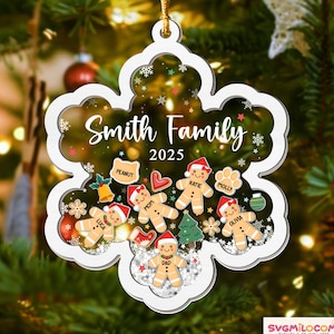 May include: A white, snowflake-shaped Christmas ornament with the text "Smith Family 2025." The ornament features gingerbread people with names, festive icons, and a gold string for hanging. The background shows a Christmas tree.