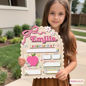 Peut inclure: Une plaque en bois festonn&eacute;e portant le pr&eacute;nom Emilia en rose, avec le texte First Day Of, une grande pomme rose et des champs vides pour la date, la taille, l'enseignant et les centres d'int&eacute;r&ecirc;t, d&eacute;cor&eacute;e de fleurs, d'un n&oelig;ud et d'ic&ocirc;nes.