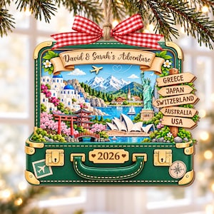May include: A green suitcase-shaped ornament with a red and white gingham bow. It features a travel scene with landmarks, a signpost reading GREECE, JAPAN, SWITZERLAND, AUSTRALIA, USA, and text reading David & Sarah's Adventure and 2026.