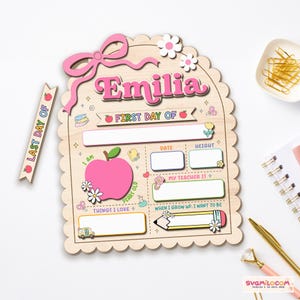 Peut inclure: Un tableau scolaire en bois &agrave; bord festonn&eacute;, portant le pr&eacute;nom Emilia en rose, une grande pomme rose et des sections pour la date, la taille, l'enseignant et les objectifs futurs. Inclut une bandelette en bois marqu&eacute;e Last Day Of.