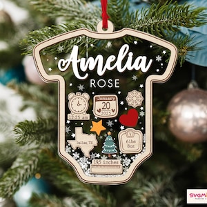 May include: A clear, onesie-shaped acrylic ornament with a wooden border and red ribbon. It features the name Amelia Rose, a clock showing 12:25 am, a calendar for January 20, 2025, a Texas map, a Christmas tree, a heart, and a scale reading 6lbs 8oz.