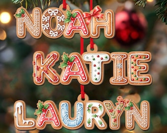 May include: Gingerbread-style Christmas ornaments spelling out the names Noah, Katie, and Lauryn. Each name is crafted with icing details, holly accents, and red ribbon hangers, set against a blurred Christmas tree backdrop.
