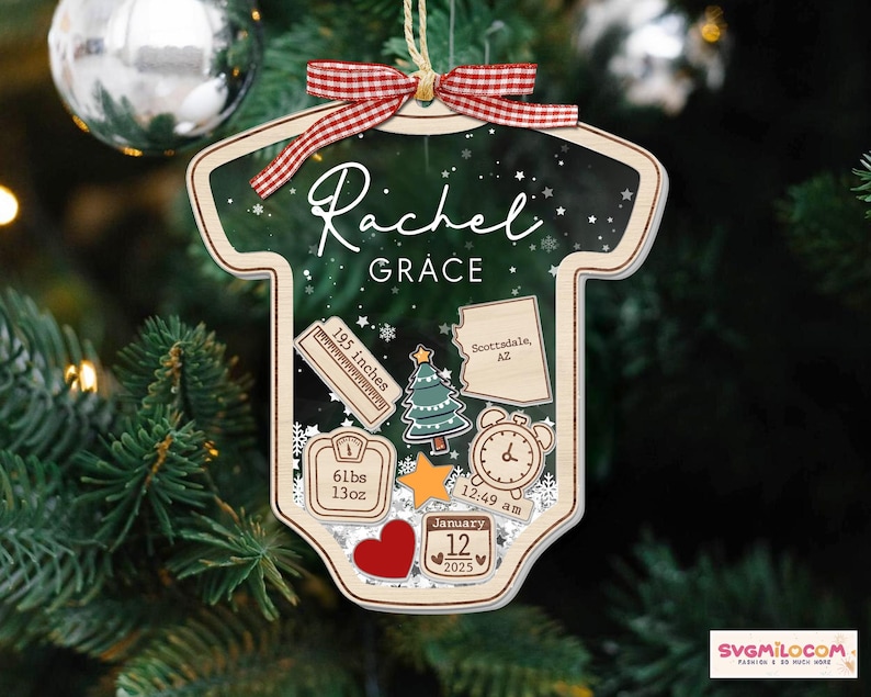 May include: A baby onesie-shaped Christmas ornament made of wood with a dark green background featuring white snowflakes. It displays the name Rachel Grace, a ruler labeled 195 inches, a map of Arizona, a tree, a scale reading 61lbs 13oz, a clock, a star, a heart, and a calendar date of January 12 2025, topped with a red and white gingham ribbon.