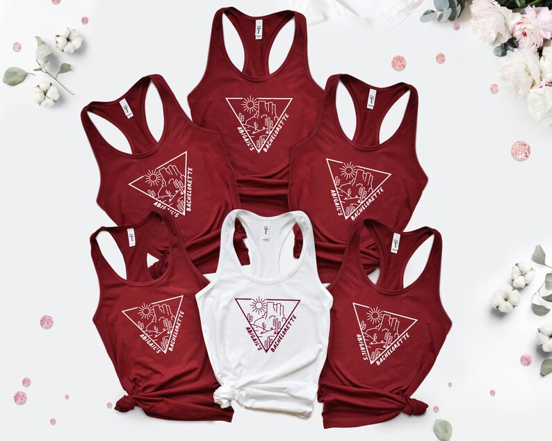 May include: Six tank tops with a white triangle design featuring a desert landscape and the text "Bride's Bachelorette". The tank tops are maroon and white.