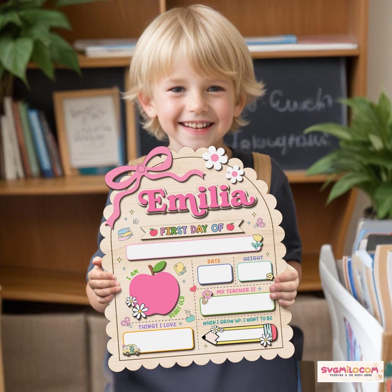 Peut inclure: Une plaque en bois clair &agrave; bord festonn&eacute; portant le pr&eacute;nom Emilia en lettres roses. La plaque comprend des sections pour First Day Of, Date, Height, My Teacher Is, Things I Love et When I Grow Up, I Want To Be, avec des illustrations.