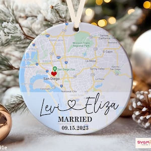 May include: A white and blue round ornament with a map of San Diego, California. The names "Levi" and "Eliza" are written in cursive with a heart symbol between them. The text "MARRIED 09.15.2023" is printed below the names.