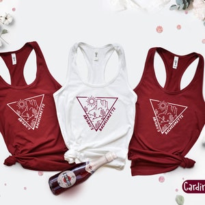 May include: Three red tank tops with white text and a graphic of a desert scene with the words "Abigail's Bachelorette" on each. The tank tops are on a white background with a bottle of sparkling wine and pink confetti.
