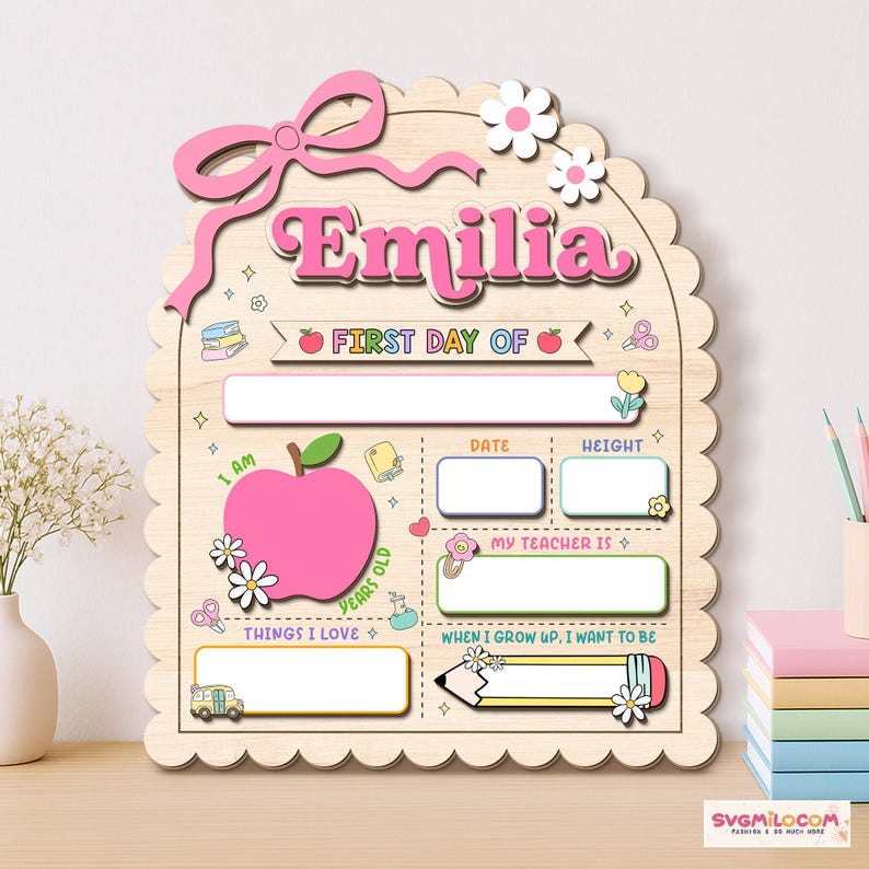 Peut inclure: Une plaque en bois festonn&eacute;e portant le nom Emilia en rose, avec une grande pomme rose, des champs vides pour la date, la taille, le professeur et les centres d'int&eacute;r&ecirc;t, d&eacute;cor&eacute;e d'un n&oelig;ud rose, de fleurs, d'un bus scolaire et d'un crayon.