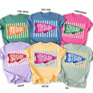 May include: Six short-sleeved crew neck t-shirts in light green, blue jean, crunchberry, orchid, butter, and bay colors. Each shirt features a graphic of a pennant flag with grade level text and the name Mrs. Sarah printed in a script font.