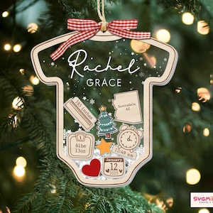 May include: A clear acrylic ornament shaped like a baby bodysuit, featuring a red and white gingham ribbon. It displays the name Rachel Grace, a ruler marked 195 inches, a map of Arizona, a Christmas tree, a scale reading 61lbs 13oz, a clock, and a calendar.