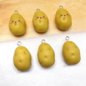 Może przedstawiać: Sześć żółtych charmów w kształcie ziemniaka ze słodkimi buźkami, każdy z srebrną pętelką do zawieszenia. Charmsy są wykonane z polimerowej gliny i idealnie nadają się do dodania odrobiny fantazji do biżuterii lub rękodzieła.