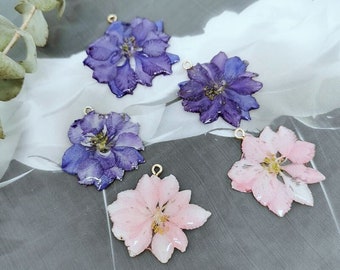 May include: Five resin flower charms with gold jump rings. Two charms are purple, two are pink, and one is a light pink. The charms are shaped like flowers with multiple petals.