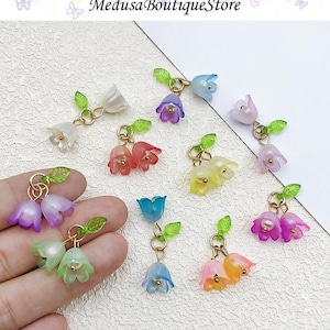May include: A collection of colorful, translucent flower earrings. Each earring features two bell-shaped flowers in shades of white, pink, purple, yellow, and blue, with green leaf accents and gold-colored metal findings. The earrings are delicate and whimsical.