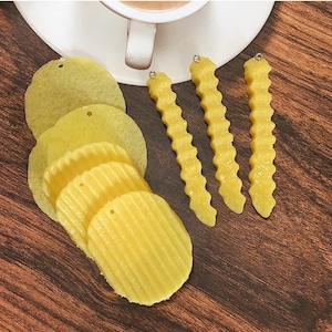 Op de afbeelding: Een set van drie paar oorbellen met een geel, golvend, frietjes-ontwerp en een set van vier paar oorbellen met een geel, rond, chips-ontwerp.