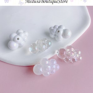 May include: Four iridescent cloud-shaped beads, two white and two clear, on a white surface.  Medusa Boutique Store is written in the background.