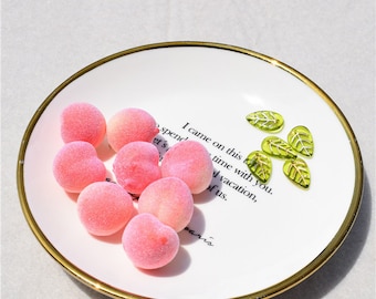 Può includere: Un piatto bianco con bordo dorato contiene oggetti rosa a forma di pesca e decorazioni verdi a forma di foglia. Il piatto presenta il testo "I came on this vacation, spend time with you, of us, paris."