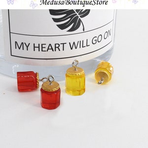 May include: Four miniature glass jars with gold lids and silver jump rings. Two jars are red and two jars are yellow.