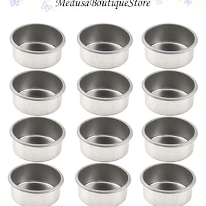 May include: Twelve silver-colored metal candle holders. Each holder is round and has a smooth, shiny surface. The holders are arranged in four rows of three.