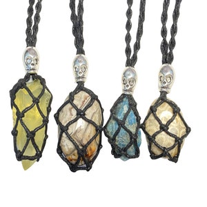 May include: Four gemstone pendants with black macrame netting and skull-shaped silver-tone metal accents. The gemstones are yellow, brown and white, blue, and beige. Each pendant hangs from a black cord.