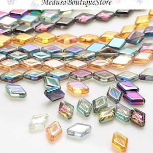 May include: Assortment of iridescent glass diamond-shaped beads in various colors, including blue, green, purple, and gold. The beads are scattered on a white surface.